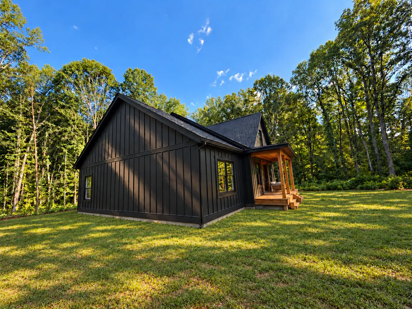 After: the cabin with a black exterior, a wood porch, and green grass, surrounded by trees.